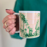 Person holding a mug with a palm tree design against a green background