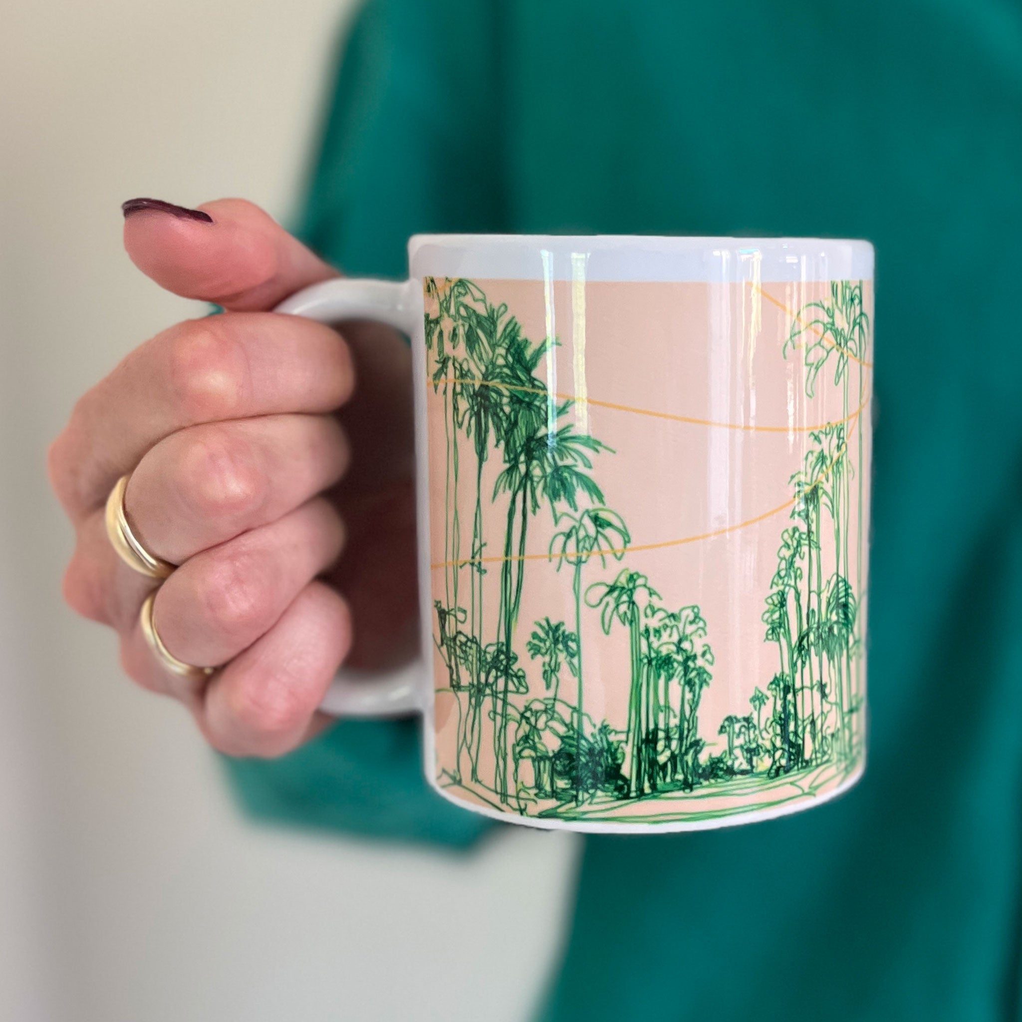 Person holding a mug with a palm tree design against a green background
