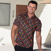 A smiling man wearing a short-sleeve button-up shirt with a colorful geometric pattern, standing outdoors in front of a modern white building.