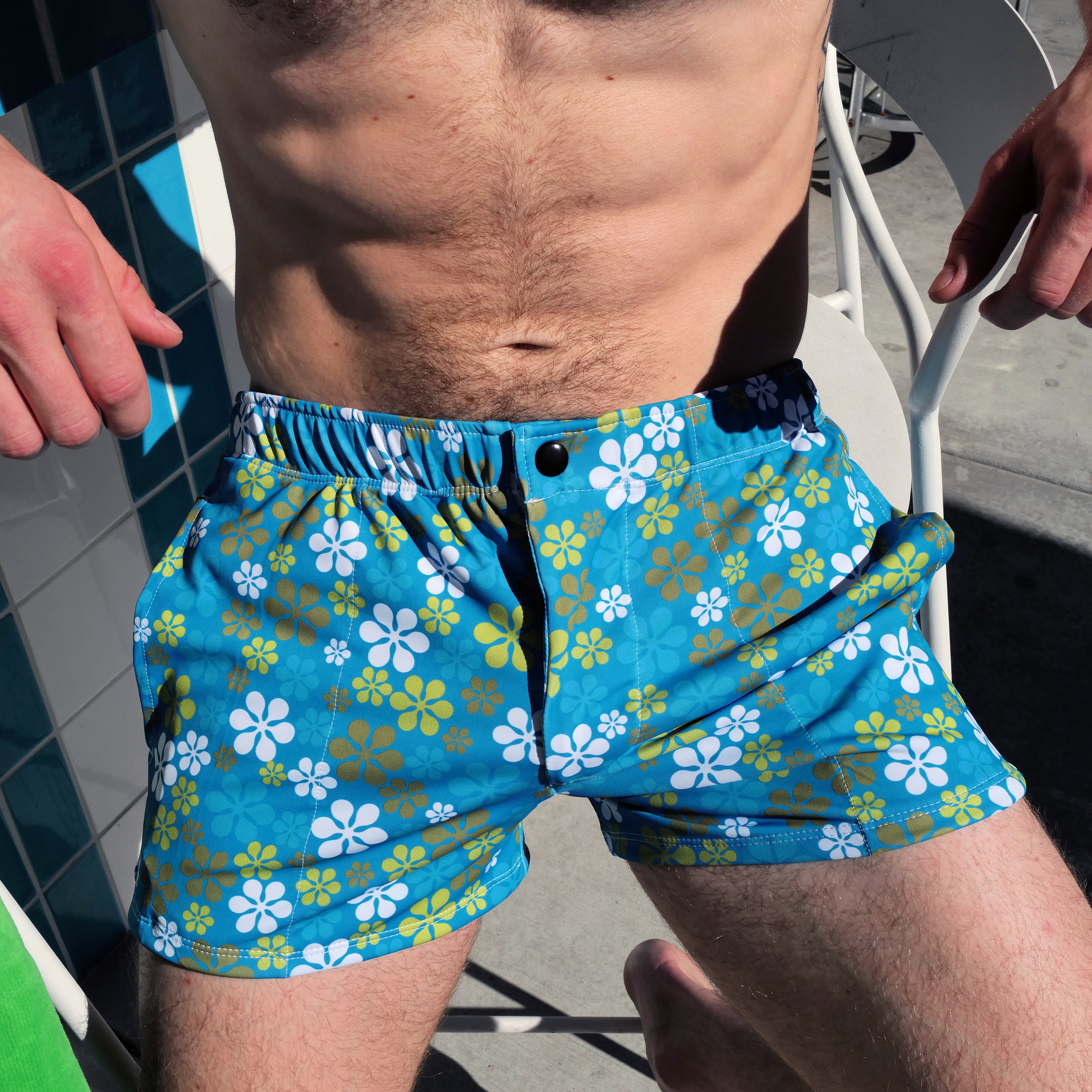 Men's swim trunks with a blue, yellow, and white floral pattern, worn by a model in an outdoor setting.