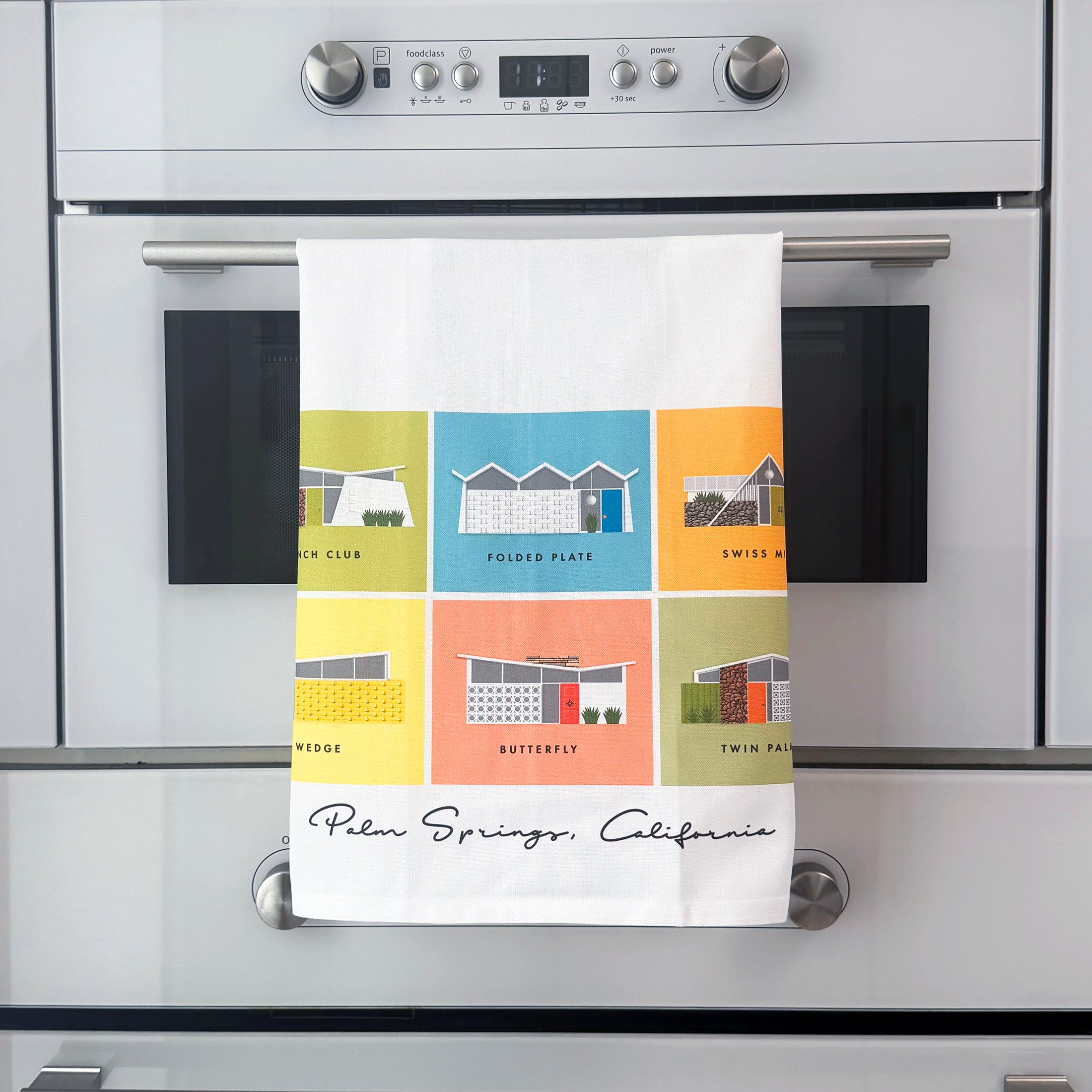 Colorful towel with midcentury Palm Springs architectural designs hanging on a kitchen oven.