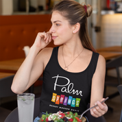 Woman wearing a black tank top with 'Palm Springs' text, sitting at a table in a casual setting.