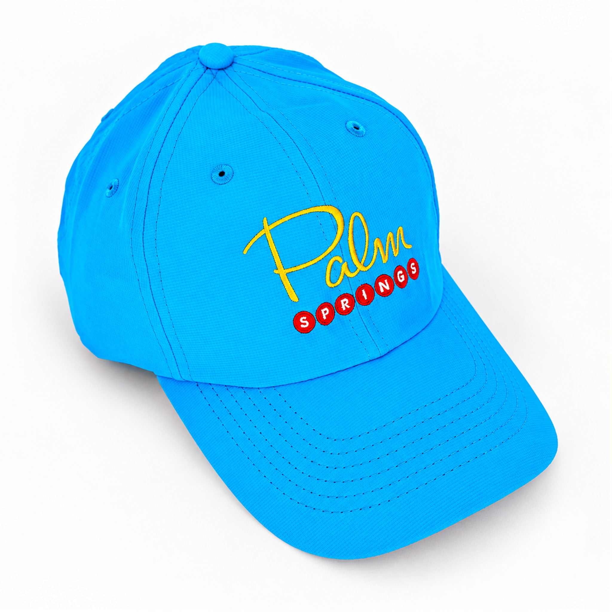 A bright blue baseball cap with 'Palm Springs' embroidered on the front, featuring yellow cursive 'Palm' and red block letters for 'Springs', shown on a clean white background.