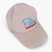 A light beige baseball cap with 'Palm Springs' embroidered on the front in blue and red, shown on a clean white background.