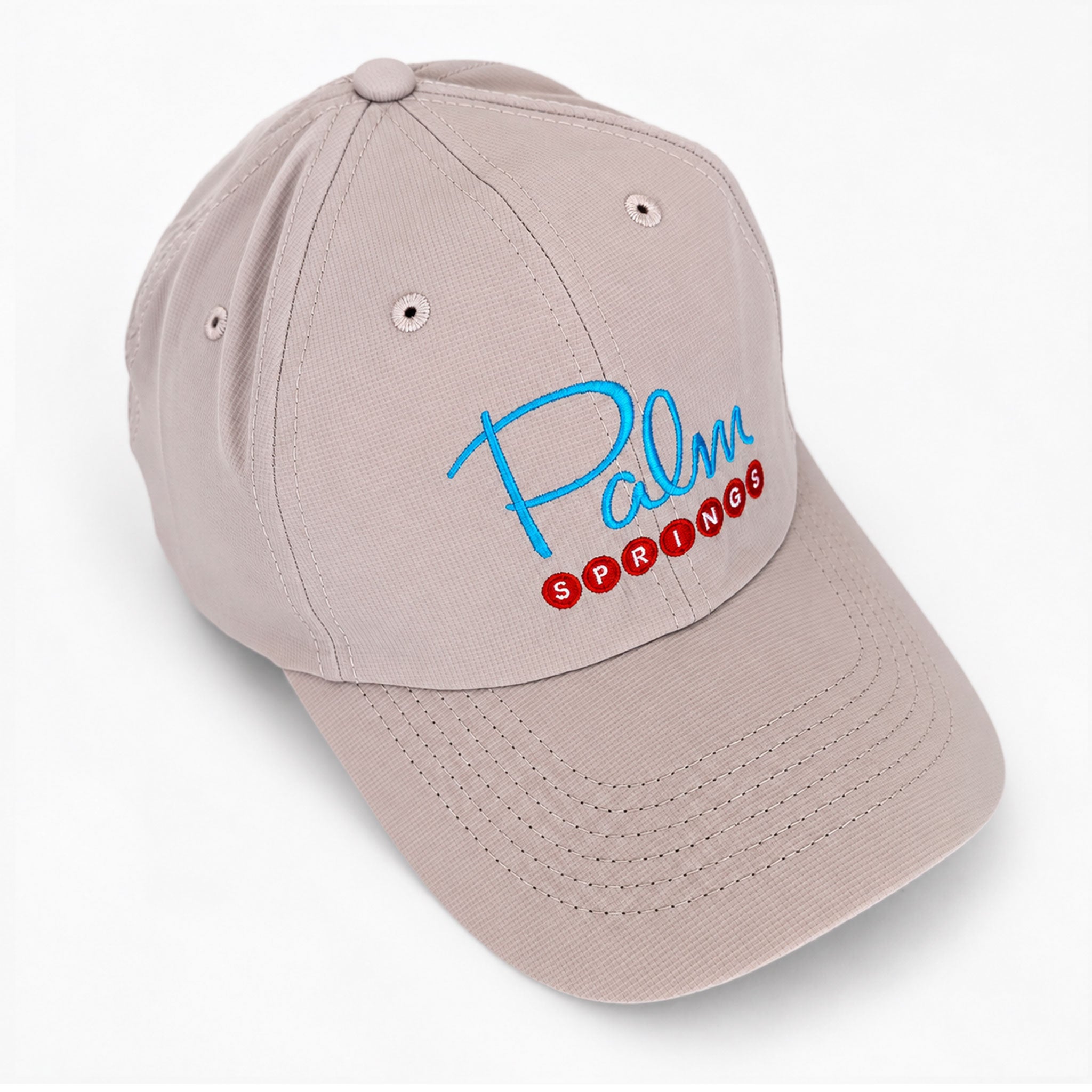 A light beige baseball cap with 'Palm Springs' embroidered on the front in blue and red, shown on a clean white background.