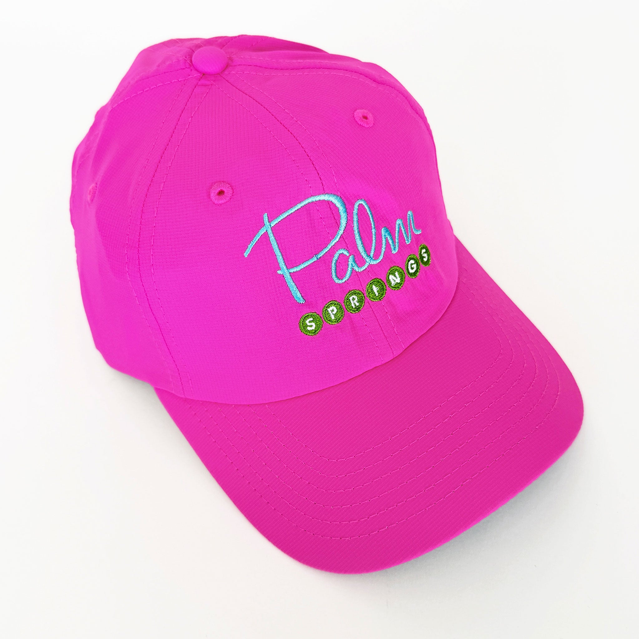 A bright pink baseball cap with 'Palm Springs' embroidered on the front in light blue and green, shown on a clean white background.