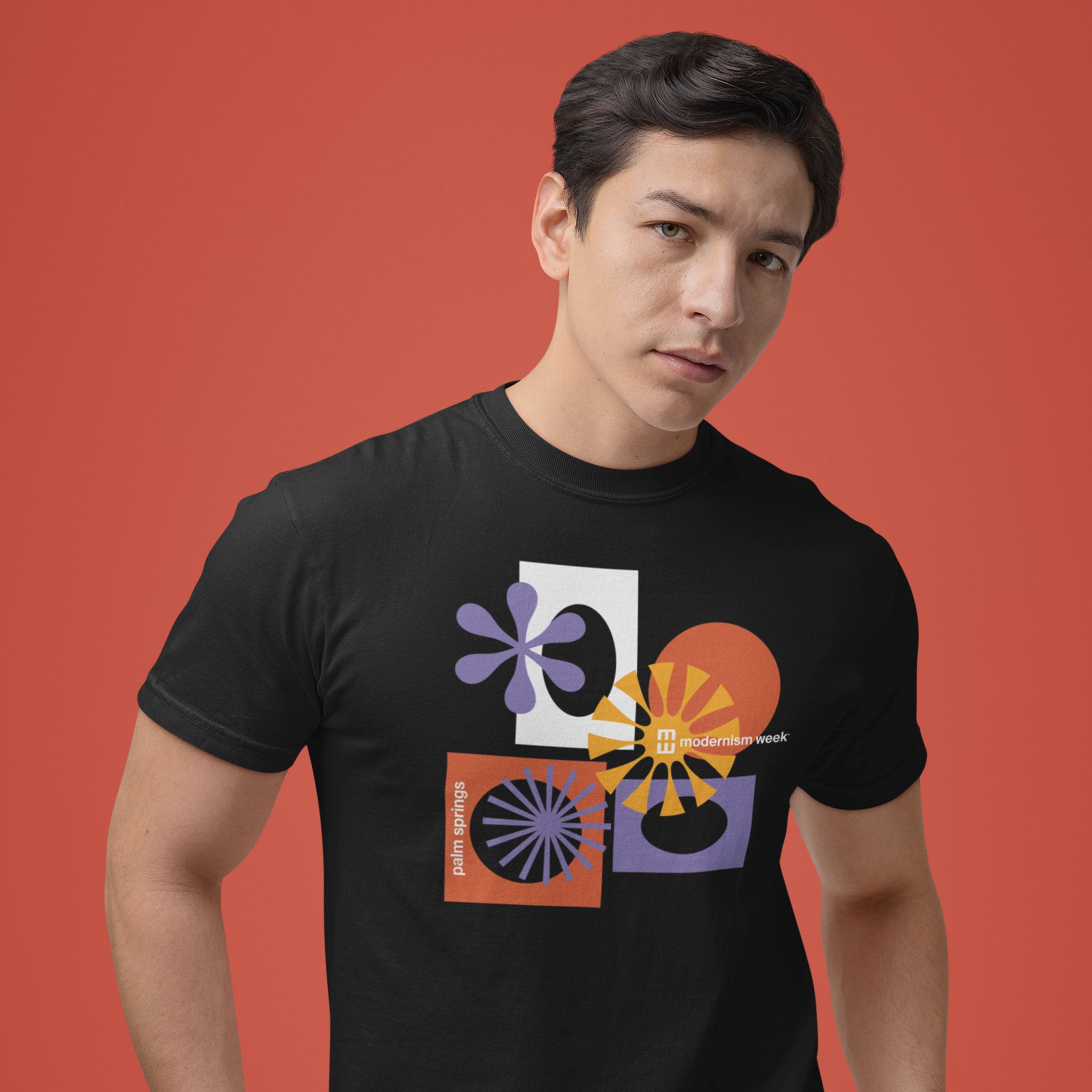 A man wearing a black t-shirt with a retro mid-century modern geometric graphic print, posed against a solid terracotta red background.