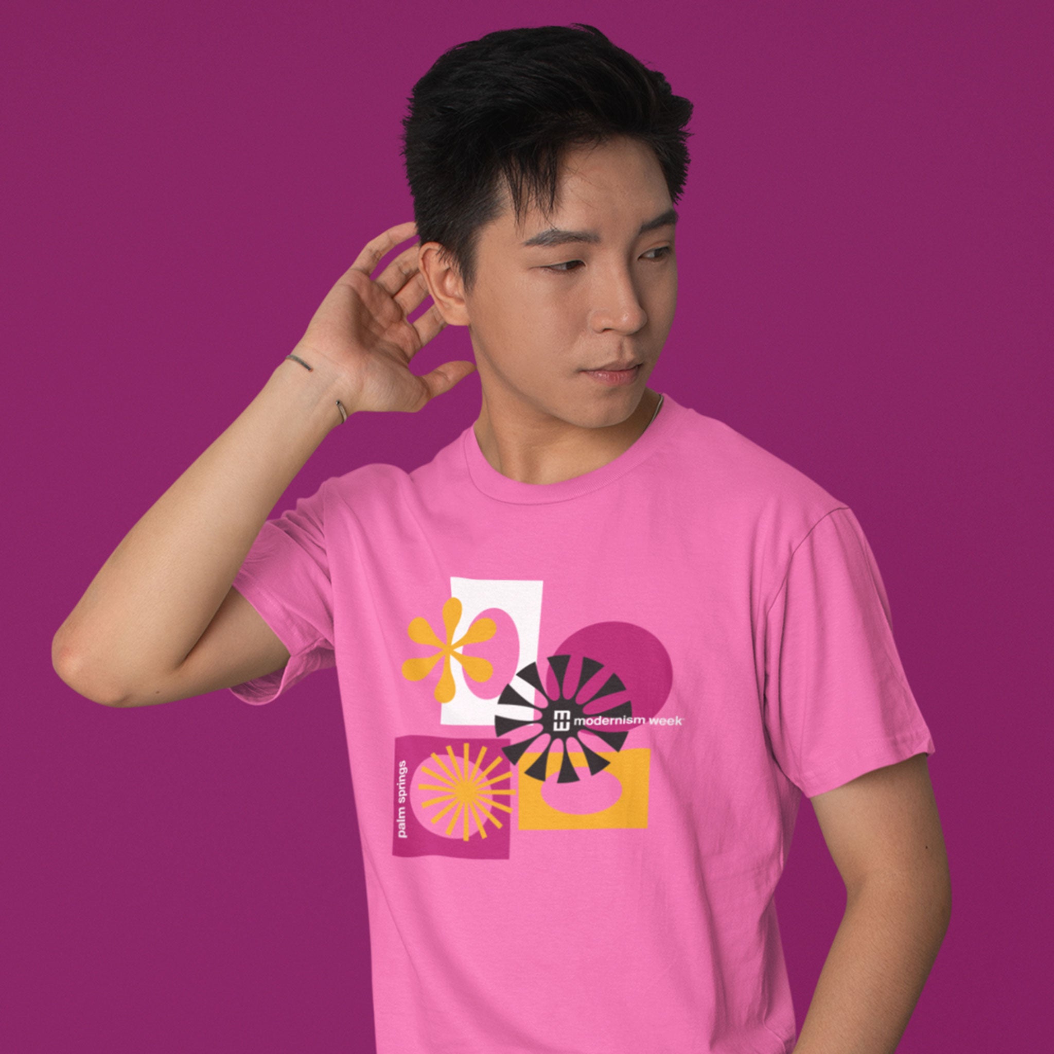 A man wearing a pink t-shirt with a retro geometric graphic print, posed against a solid magenta background.