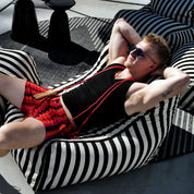 Man lounging on a black and white striped bean bag chair wearing sunglasses and red shorts.