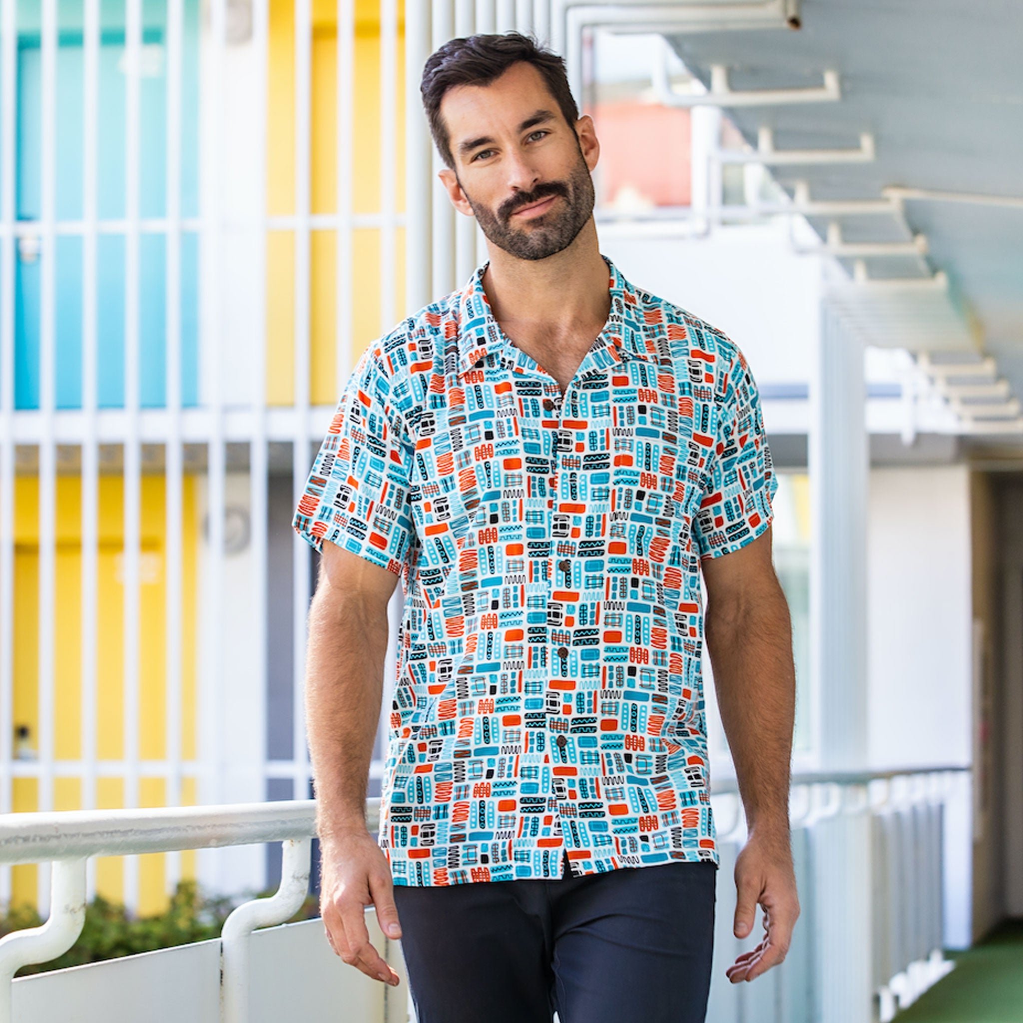 Man facing forward wearing a colorful mod patterned button-down shirt on a Palm Springs hotel balcony.