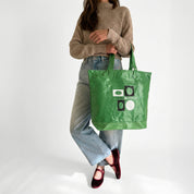 Person holding a green tote bag with graphic design on a white background