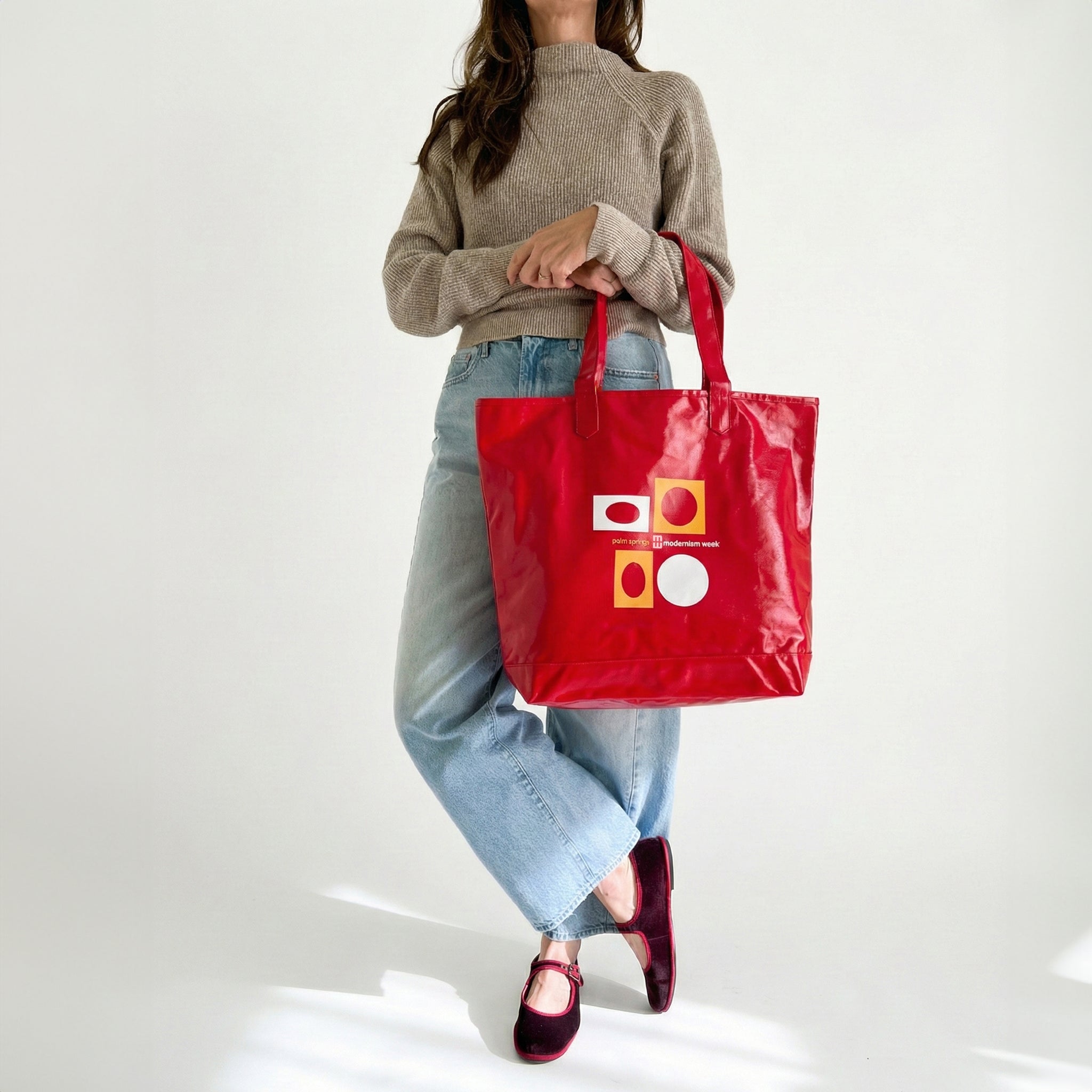 Person holding a red tote bag with geometric patterns on a white background