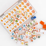 A set of colorful card game blocks and dice displayed on a white surface, with an open clear plastic storage case showing the organized pieces and several loose pieces scattered around.