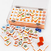 A clear plastic case filled with Mahjong tiles, with several loose tiles and two blue dice scattered in front on a white background.