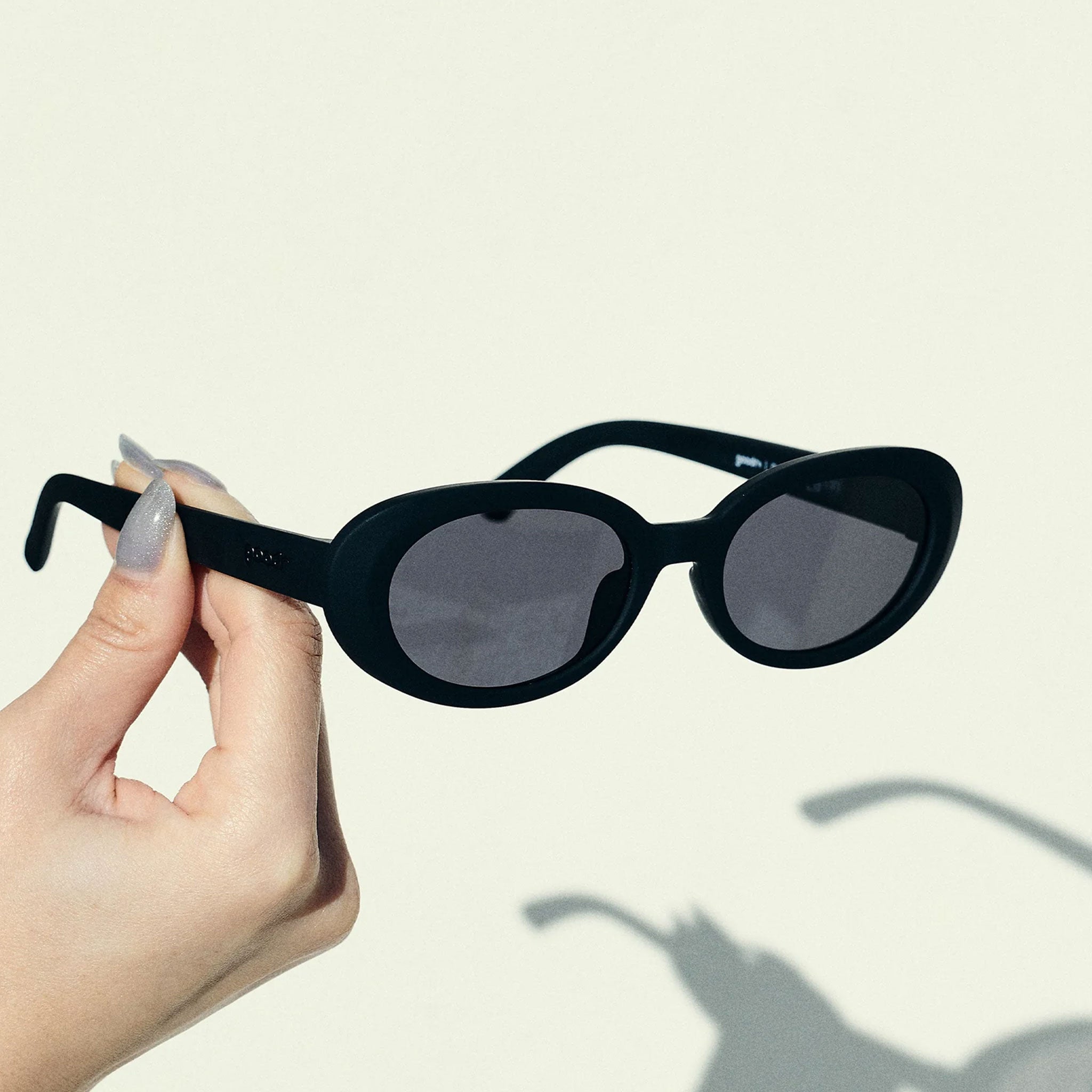 Black sunglasses held by a hand against a light background