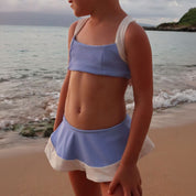 Person wearing a blue and white outfit standing on a beach with ocean waves in the background