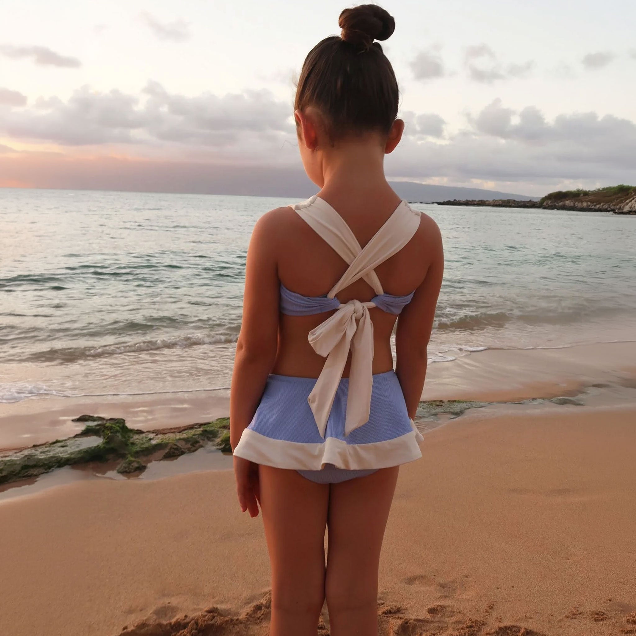 Person in a blue and white swimsuit standing on a beach with ocean view