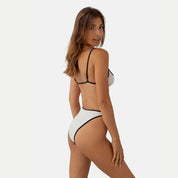 A rear view of a woman wearing a kya reversible swimsuit in oat color.