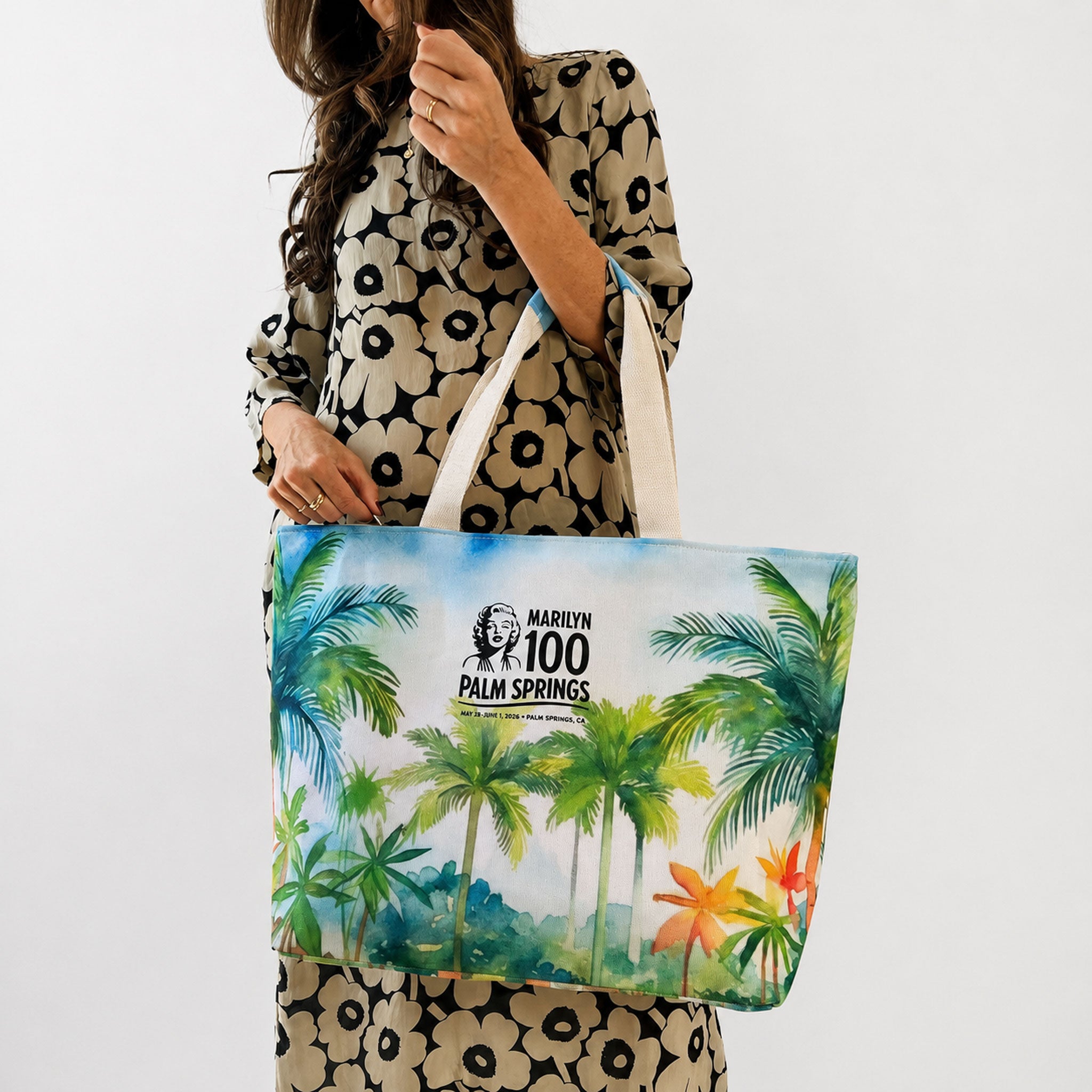 Tote bag with palm tree design held by a person wearing a floral dress.