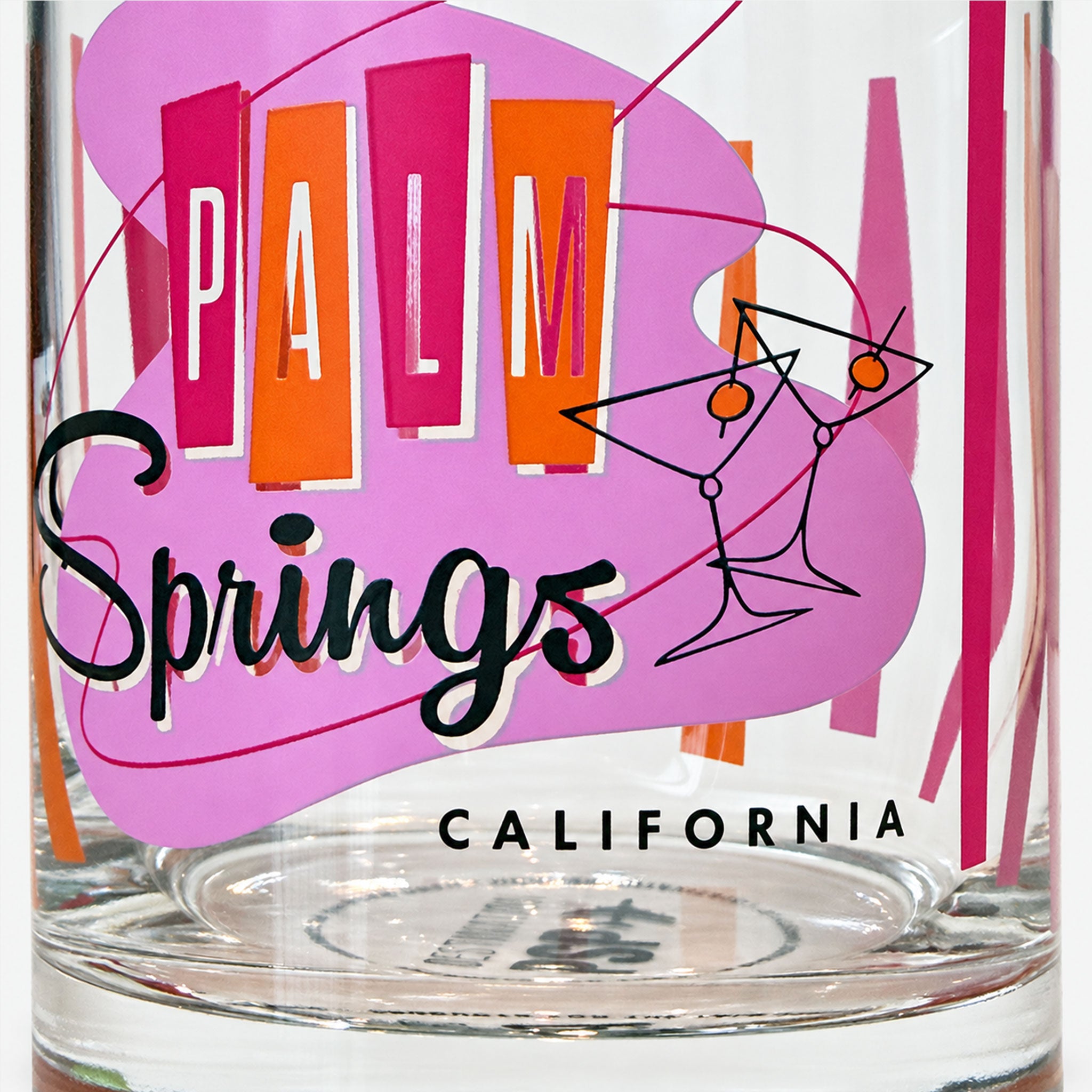 A clear glass tumbler featuring a colorful retro-style 'Palm Springs California' graphic with pink, orange, and black lettering and line art.