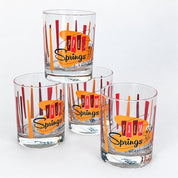 Four clear glass tumblers with a vintage-style 'Palm Springs California' print, featuring orange and red abstract shapes and black script, arranged on a white background.