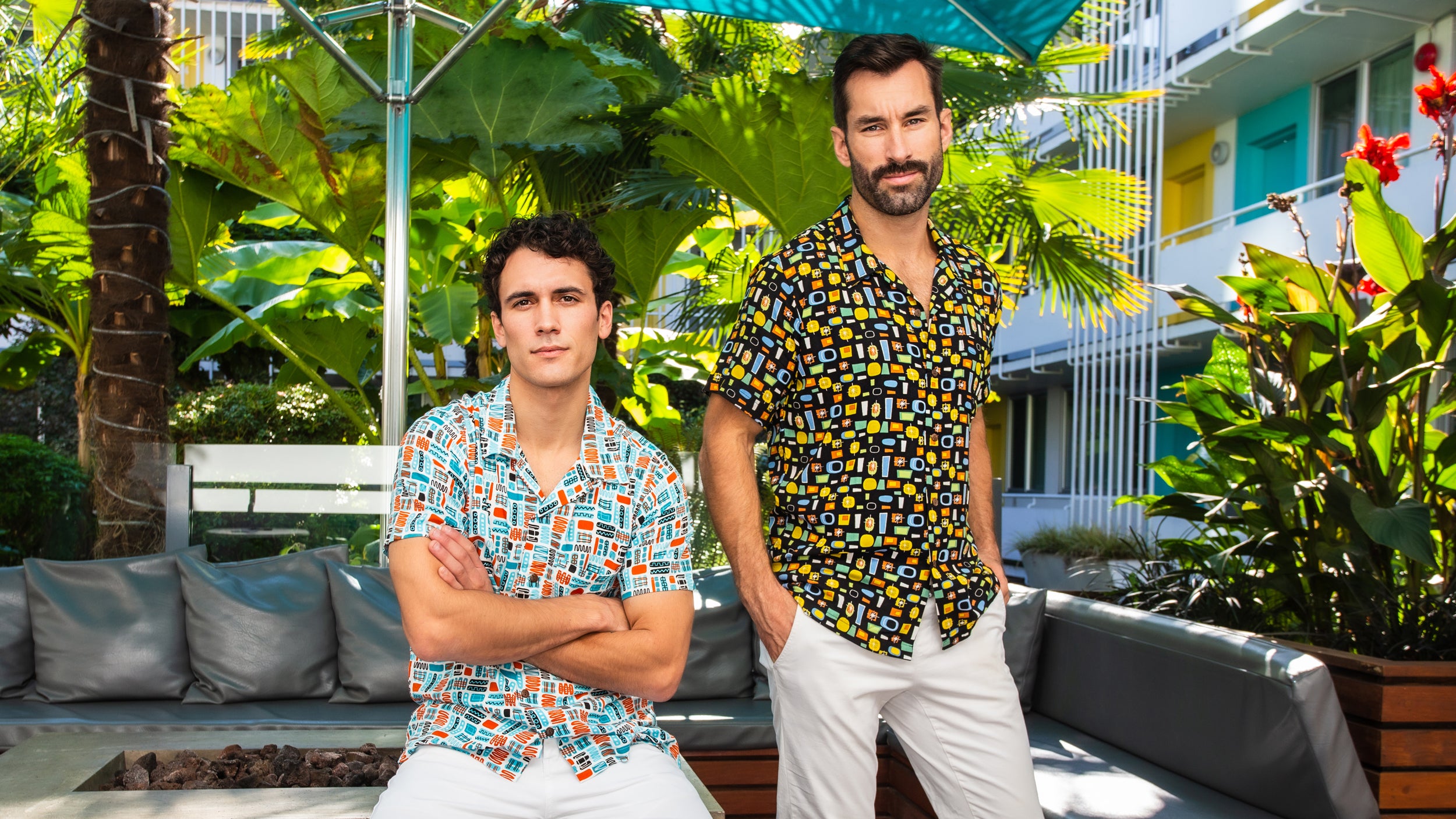 Two men in vibrant resort shirts standing on a patio with a scenic Palm Springs hotel backdrop, exuding vacation vibes.