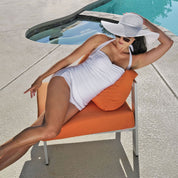 Woman in a white swimsuit and sun hat lounging on an orange chair by a pool.
