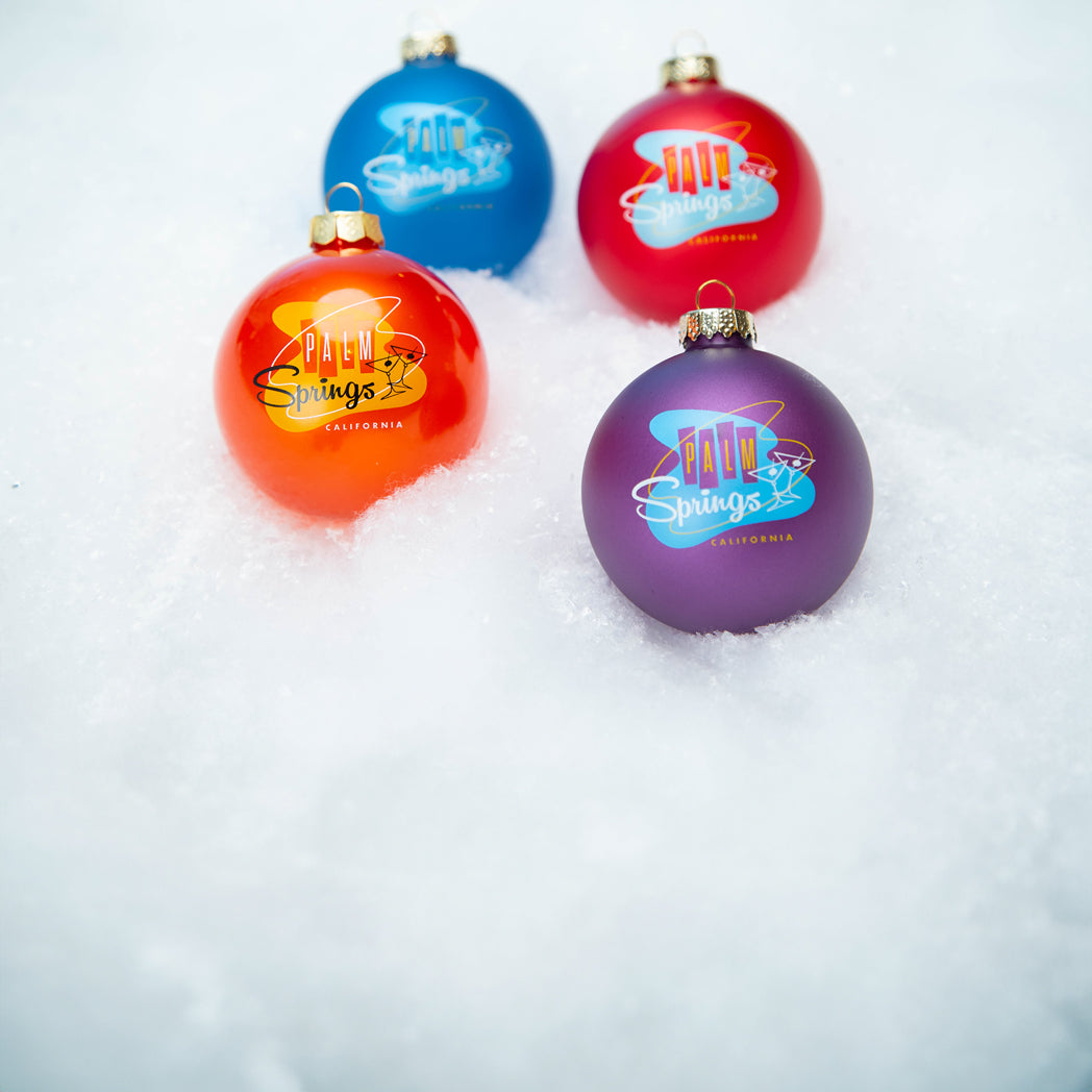 A set of four glass Christmas ornaments placed delicately on a bed of fake snow.