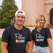 Two people wearing black t-shirts with 'Palm Springs' printed on them, sitting outdoors.