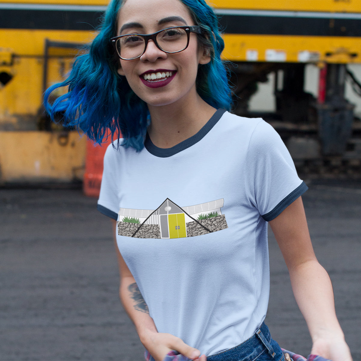 Smiling girl with blue hair and glasses walking on street wearing jeans and T-shirt.